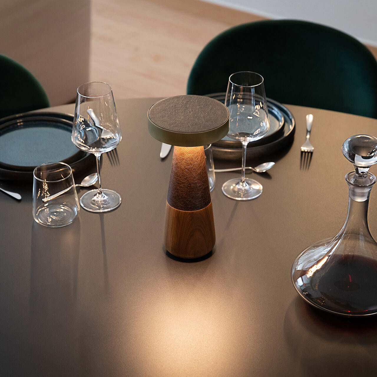 a close up on a wooden black round table that on top of it it has an open table wooden dark brown lamp three drink glasses four of various size round plates and a wine glass filled decanter