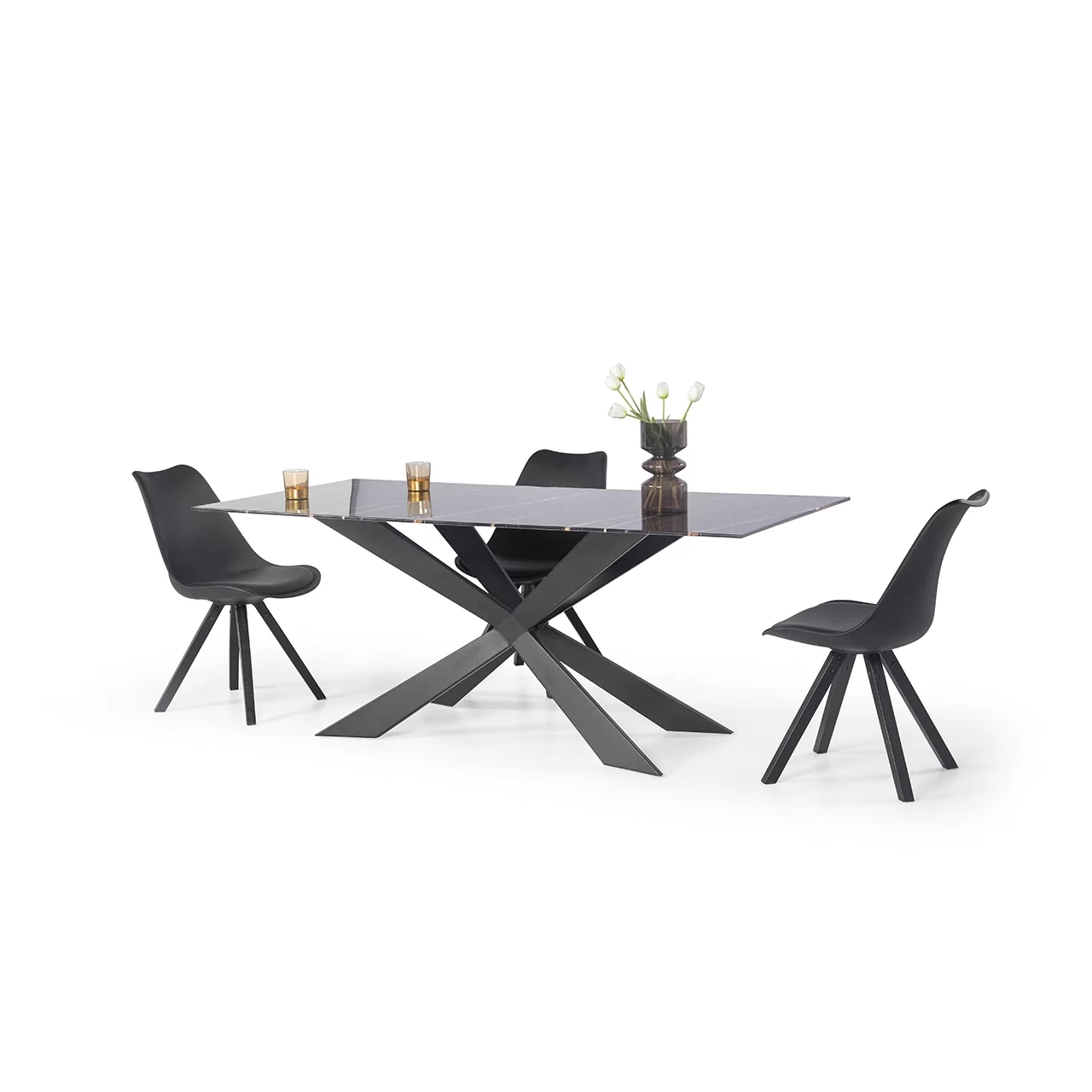 a glass black table with its legs forming an x surrounded by three black chairs and on top of the table are two glasses and a vase